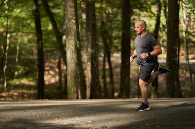 Güneşli bir antrenman sırasında asfalt yolda koşan atletik bir adam.