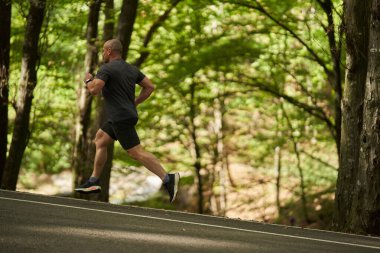 Güneşli bir antrenman sırasında asfalt yolda koşan atletik bir adam.