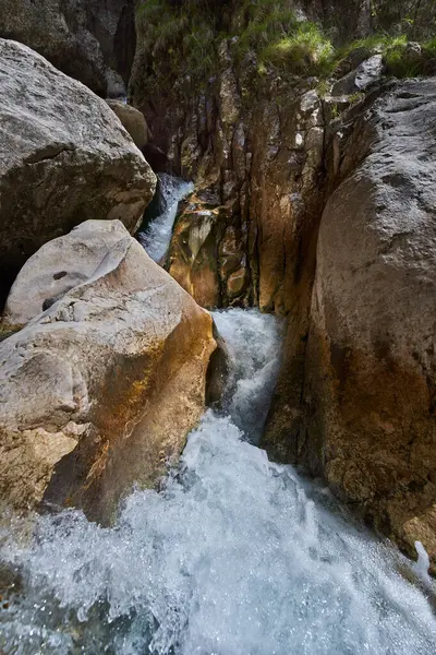 Dik taş oluşumlarından akan suyla dar kayalık vadi.