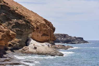 İspanya, Kanarya Adaları, Tenerife, 06 Mayıs 2025 - İnsanlar Tenerife 'deki Playa de Montana Amarilla' da volkanik kayalıkların yakınında güneşleniyor ve yüzüyorlar