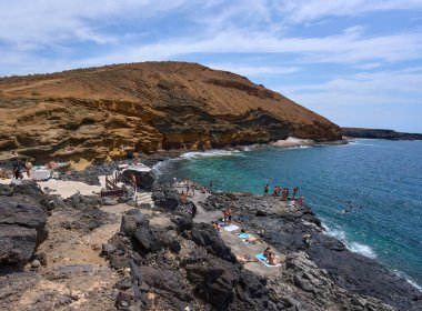 İspanya, Kanarya Adaları, Tenerife - 6 Mayıs 2025: İnsanlar Tenerife 'deki Playa de Montana Amarilla' da volkanik kayalıkların yakınında güneşleniyor ve yüzüyorlar