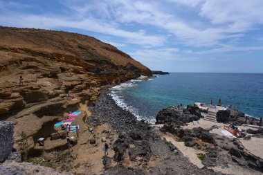 İspanya, Kanarya Adaları, Tenerife - 6 Mayıs 2025: İnsanlar Tenerife 'deki Playa de Montana Amarilla' da volkanik kayalıkların yakınında güneşleniyor ve yüzüyorlar