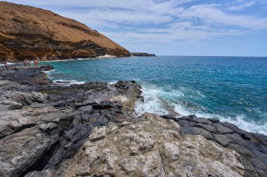 İspanya, Kanarya Adaları, Tenerife - 6 Mayıs 2025: İnsanlar Tenerife 'deki Playa de Montana Amarilla' da volkanik kayalıkların yakınında güneşleniyor ve yüzüyorlar