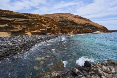İspanya, Kanarya Adaları, Tenerife - 6 Mayıs 2025: İnsanlar Tenerife 'deki Playa de Montana Amarilla' da volkanik kayalıkların yakınında güneşleniyor ve yüzüyorlar