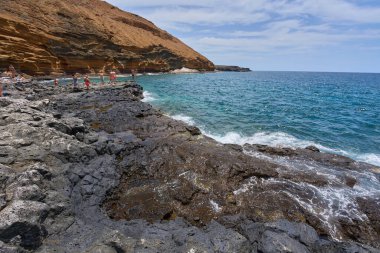 İspanya, Kanarya Adaları, Tenerife - 6 Mayıs 2025: İnsanlar Tenerife 'deki Playa de Montana Amarilla' da volkanik kayalıkların yakınında güneşleniyor ve yüzüyorlar