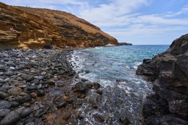 İspanya, Kanarya Adaları, Tenerife - 6 Mayıs 2025: İnsanlar Tenerife 'deki Playa de Montana Amarilla' da volkanik kayalıkların yakınında güneşleniyor ve yüzüyorlar