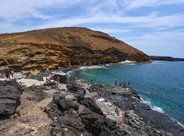 İspanya, Kanarya Adaları, Tenerife - 6 Mayıs 2025: İnsanlar Tenerife 'deki Playa de Montana Amarilla' da volkanik kayalıkların yakınında güneşleniyor ve yüzüyorlar