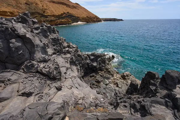 Tenerife 'deki Playa de Montana Amarilla yakınlarında volkanik kıyı şeridi ve okyanus dalgaları çarpışıyor. 