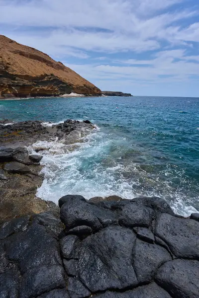Tenerife 'deki Playa de Montana Amarilla yakınlarında volkanik kıyı şeridi ve okyanus dalgaları çarpışıyor. 