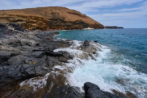 İspanya, Kanarya Adaları, Tenerife - 6 Mayıs 2025: İnsanlar Tenerife 'deki Playa de Montana Amarilla' da volkanik kayalıkların yakınında güneşleniyor ve yüzüyorlar