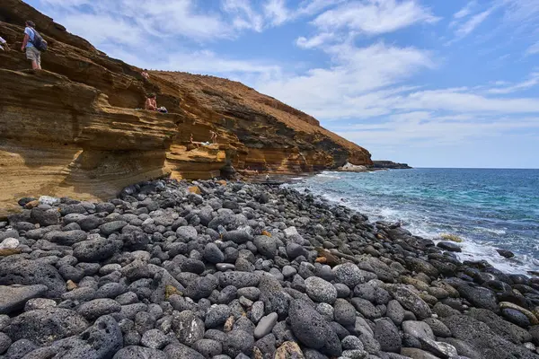 İspanya, Kanarya Adaları, Tenerife - 6 Mayıs 2025: İnsanlar Tenerife 'deki Playa de Montana Amarilla' da volkanik kayalıkların yakınında güneşleniyor ve yüzüyorlar