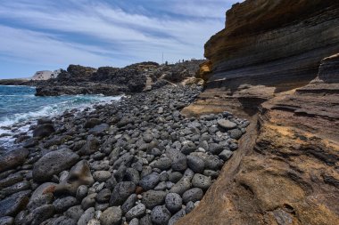 Playa de Montana Amarilla 'daki kayalık ve katmanlı volkanik kayalıklar bazalt taşlarına okyanus dalgaları çarpıyor. 