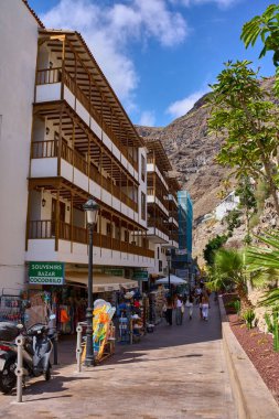 Acantilados de Los Gigantes 'teki sokak manzarasında Playa de los Guios' a giden yolda hediyelik eşya dükkanları, yayalar ve geleneksel mimariler görülüyor.