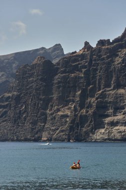 İnsanlar Tenerife 'deki Los Gigantes' in yüksek volkanik kayalıklarının altında sakin sularda kano kullanıyorlar.