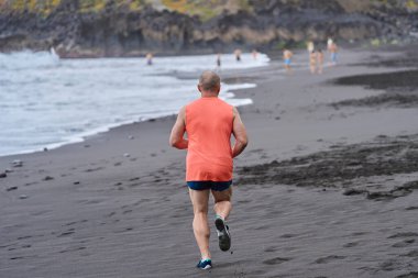 El Bollullo sahilinin kara volkanik kumları boyunca koşan bir adam.