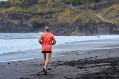 El Bollullo sahilinin kara volkanik kumları boyunca koşan bir adam.