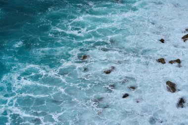 Aerial view of the rocky volcanic shoreline next to El Bollullo beach in Tenerife with foamy waves crashing over moss-covered boulders