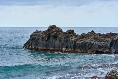 Tenerife 'deki El Bollullo plajı yakınlarındaki volkanik kaya oluşumları ve okyanus dalgalarının hava manzarası köpüklü dalgaların siyah kayalara ve yosun taşlarına çarpmasıyla