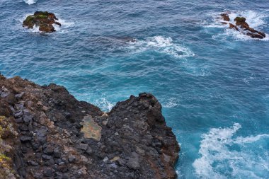 Tenerife 'deki El Bollullo plajı yakınlarındaki volkanik kaya oluşumları ve okyanus dalgalarının hava manzarası köpüklü dalgaların siyah kayalara ve yosun taşlarına çarpmasıyla