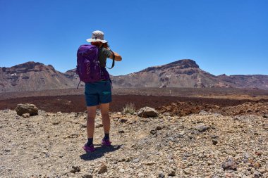 Mor sırt çantalı kadın Teide Ulusal Parkı 'ndaki engebeli kaldera kayalıklarını fotoğraflıyor.