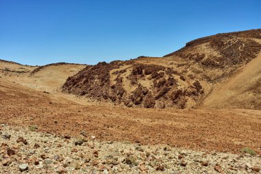 Parlak bir yaz gününde Teide yakınlarında aşınmış volkanik tepeleri kesen dolambaçlı bir yol.