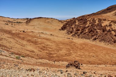 Parlak bir yaz gününde Teide yakınlarında aşınmış volkanik tepeleri kesen dolambaçlı bir yol.