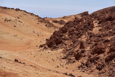 Erimiş lav oluşumlarıyla kayalık volkanik sırt ve öğlen güneşinin altında kurak yamaçlarda süzülen soluk bir iz.