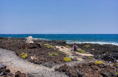 Kameralı bir kadın, Malpais de Guimar kıyısındaki volkanik arazide işaretli bir patika boyunca yürüyor. 