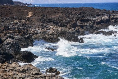 Dalgalar Tenerife Adası 'ndaki Malpais de Guimar kıyısı boyunca volkanik kayalara çarpıyor.