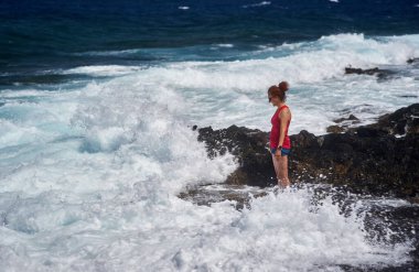 Atlantik Okyanusu dalgalarının keyfini çıkaran mutlu kızıl kadın Tenerife 'nin kayalık kıyılarına çarpıyor.