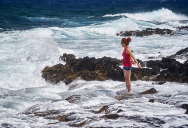 Atlantik Okyanusu dalgalarının keyfini çıkaran mutlu kızıl kadın Tenerife 'nin kayalık kıyılarına çarpıyor.