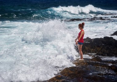 Atlantik Okyanusu dalgalarının keyfini çıkaran mutlu kızıl kadın Tenerife 'nin kayalık kıyılarına çarpıyor.