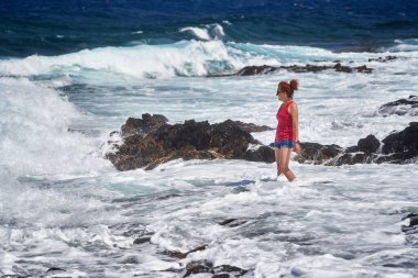 Atlantik Okyanusu dalgalarının keyfini çıkaran mutlu kızıl kadın Tenerife 'nin kayalık kıyılarına çarpıyor.