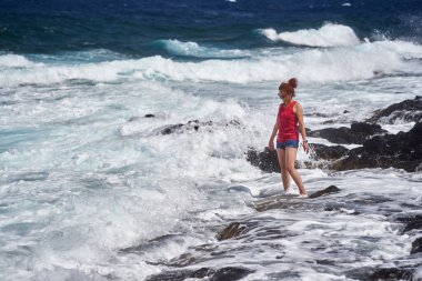 Atlantik Okyanusu dalgalarının keyfini çıkaran mutlu kızıl kadın Tenerife 'nin kayalık kıyılarına çarpıyor.