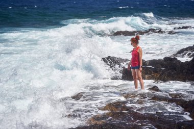 Atlantik Okyanusu dalgalarının keyfini çıkaran mutlu kızıl kadın Tenerife 'nin kayalık kıyılarına çarpıyor.