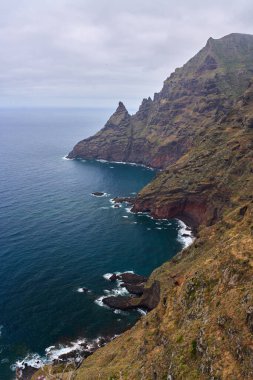 Anaga, Tenerife 'deki volkanik kıyı kayalıkları Atlantik kıyısı boyunca katmanlı katmanlar ve deniz mağaraları bulutlu gökyüzünün altında.