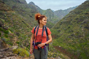 Anaga, Tenerife 'deki yeşil volkanik kanyonlarda kameralı kızıl saçlı kadın yürüyüşçü.