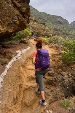 Mor sırt çantalı turist kadın Anaga dağlarında volkanik patikalara tırmanıyor.
