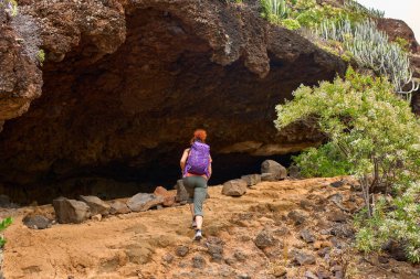 Mor sırt çantalı bir kadın Tenerife 'deki kayalık yolda volkanik mağaraya yaklaşıyor.