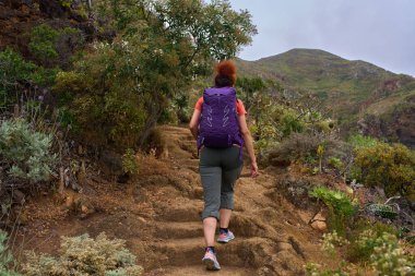 Tenerife 'nin Anaga dağlarındaki aşınmış volkanik merdivenlerde yokuş yukarı yürüyen bir kadın.