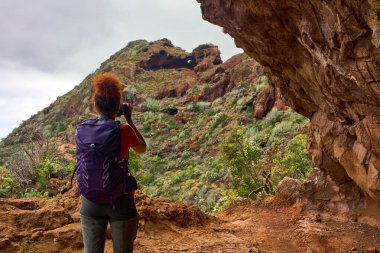 Anaga Dağları 'ndaki volkanik patikada bitki örtüsünü fotoğraflayan turist kadın.