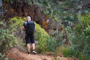 Anaga dağlarında yürüyüş yaparken sırt çantası ve kamerayla manzara fotoğraflayan bir adam.