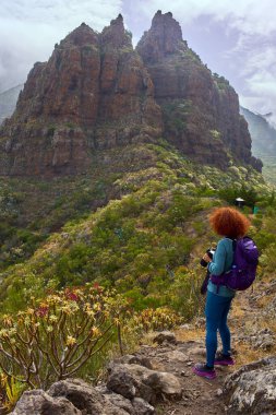 Kameralı kadın Teno dağlarındaki volkanik kayalıklara bakan patikada duruyor.