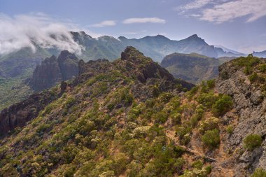 Dar yürüyüş yolları ve Tenerife 'nin Teno dağlarındaki bulutlu gökyüzünün altında dramatik volkanik tepeleri olan kurak yamaçlar.