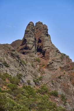 Tenerife 'nin uzak Teno bölgesinde berrak mavi bir gökyüzünün altında sivri bir volkanik zirvenin etrafında dönen dar dağ yolu.