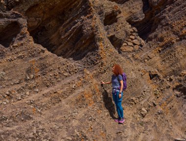 Kadın, Tenerife 'deki Teno' nun güneşli dağlarında aktif bir yürüyüş sırasında kayalık bir patikaya tırmanıyor.