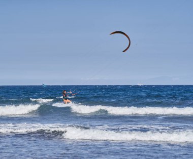 İspanya, Kanarya Adaları, Tenerife, Playa del Medano - 05 Haziran 2025: Mavi gölgelik altında açık okyanusta uçurtma uçuran genç kadın