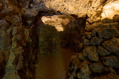 Kaba taş duvarları ve loş ışıklandırması olan eski lav tüplerinden oluşan volkanik bir mağaranın içinde.