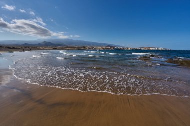 Playa del Medano, dalgalı siyah kum ve El Medano kasabası.