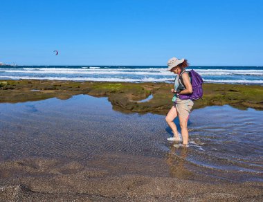Sırt çantalı bir kadın güneşli bir tatilde Playa del Medano kıyılarında sığ sularda yürüyor.